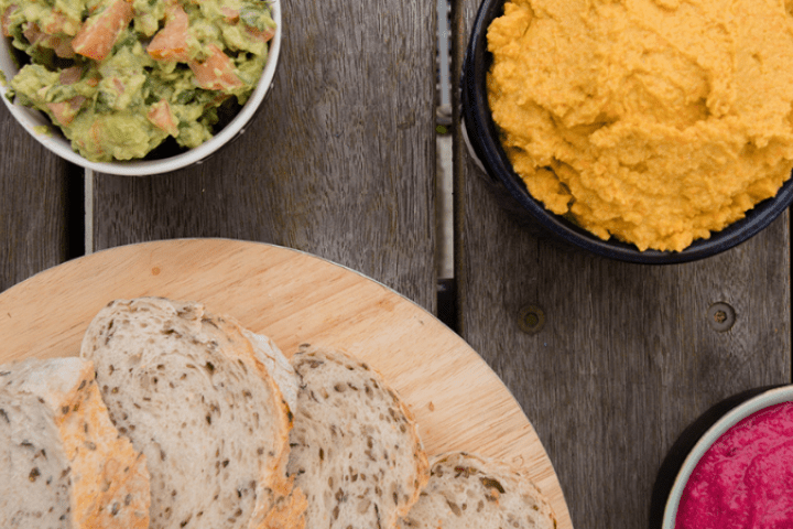 A spread of avocado, beetroot, and carrot and chickpea dips in small bowls served with a plate of bread.