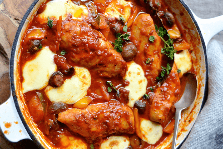 Mediterranean chicken served in a saucepan on a wooden board.