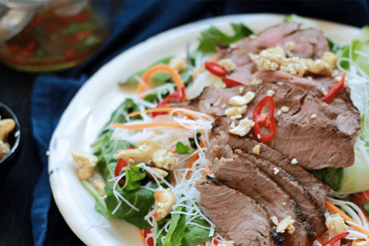 Thai beef salad on white plate and nuts on the side.