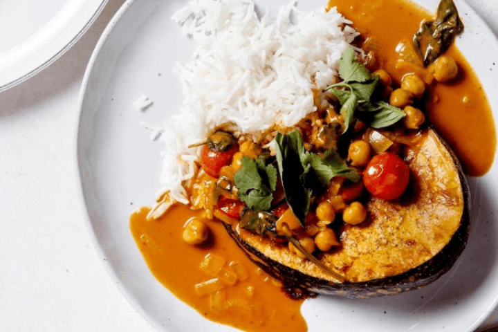 Thai pumpkin and chickpea curry served on a white plate with bread and rice.