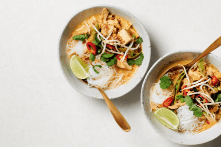 Tofu and mushroom laksa served in white bowls with forks.