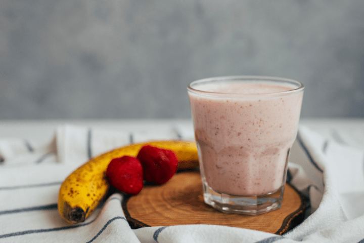 Strawberry smoothie in a glass next to a banana and some strawberries