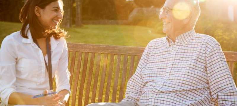 Younger woman speaking with older man on a bench outside.