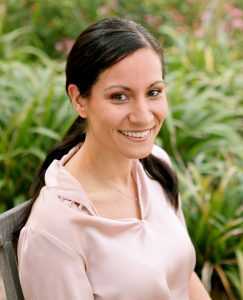 Woman with long dark hair and wearing a pink top smiles at the camera