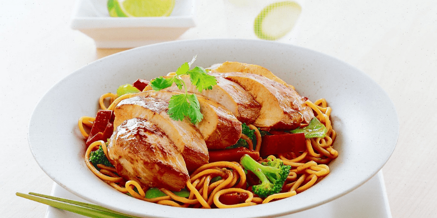 Teriyaki chicken and noodle stir fry in a white bowl with lime on the side.