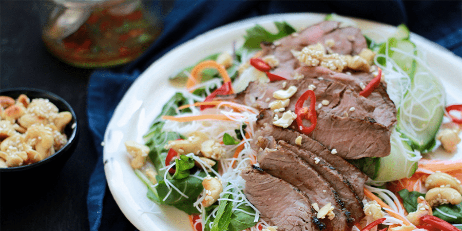 Thai beef salad on white plate and nuts on the side.