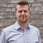 Man with brown hair and a beard looks directly at the camera