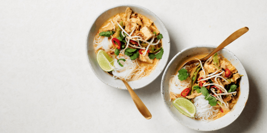 Tofu and mushroom laksa served in white bowls with forks.