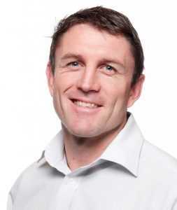 Man with short brown hair and white shirt smiling at camera