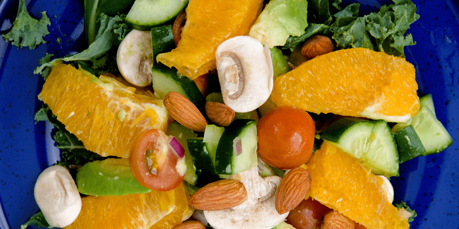 Various cut up vegetables and oranges on a blue plate