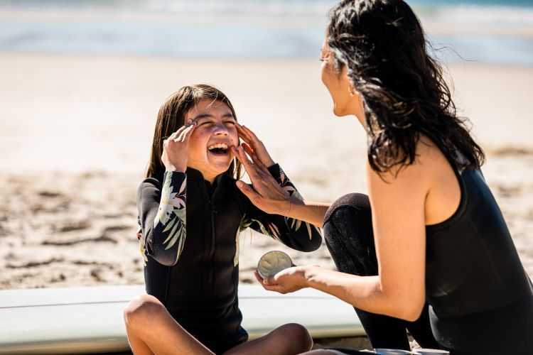 A woman applying sunscreen to daughter at the beach