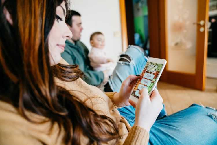 Woman searching food on her mobile sitting next to husband and baby.