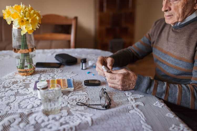 Elderly man sitting checking his diabetes with medication on table.