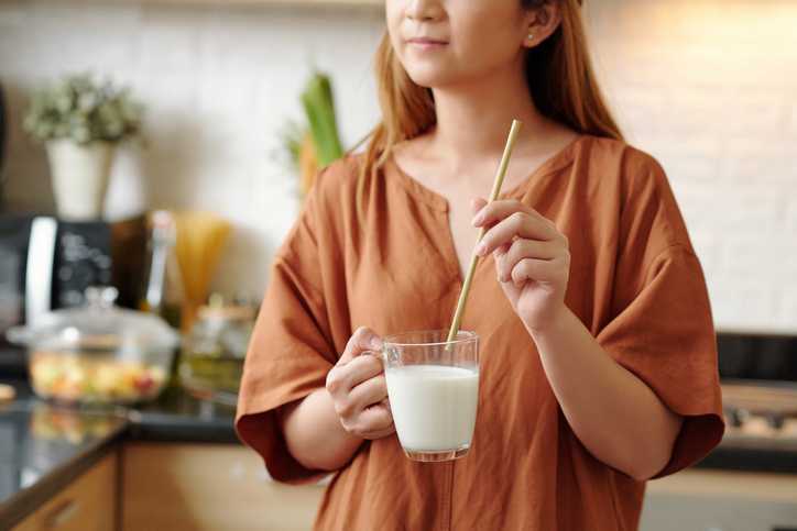 Young woman drinking cup of almond milk through biodegradable paper straw
