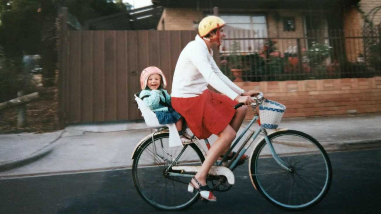a women riding a bicycle while a child is on the back in a child seat. 