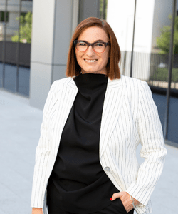 Women smiling one hand in pocket. wearing a white blazer, wearing glasses