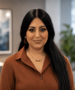 Women in office with long dark hair, smiling wearing a brown shirt.